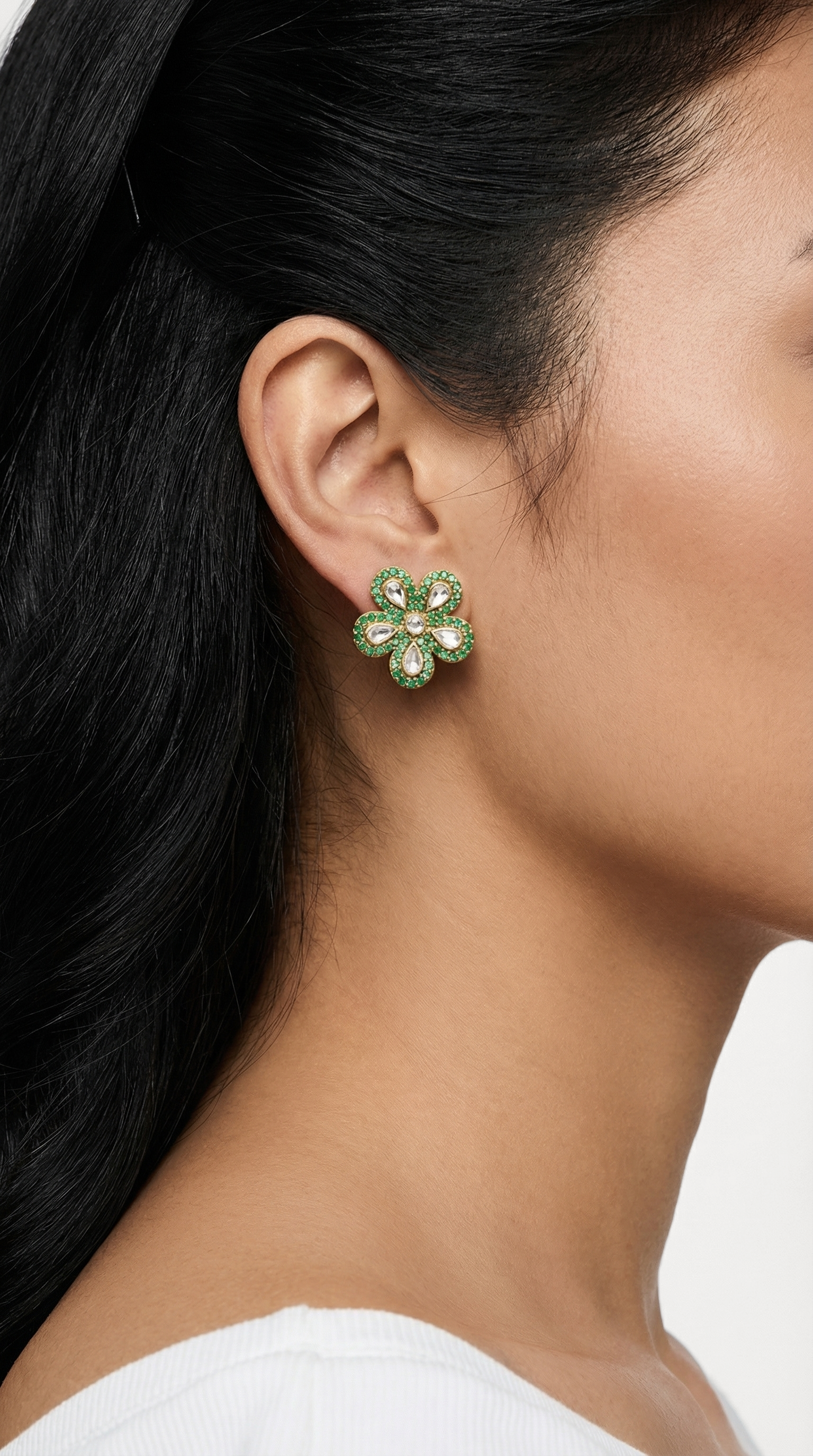 Close-up of a person wearing a green floral earring with dark hair and a white top.