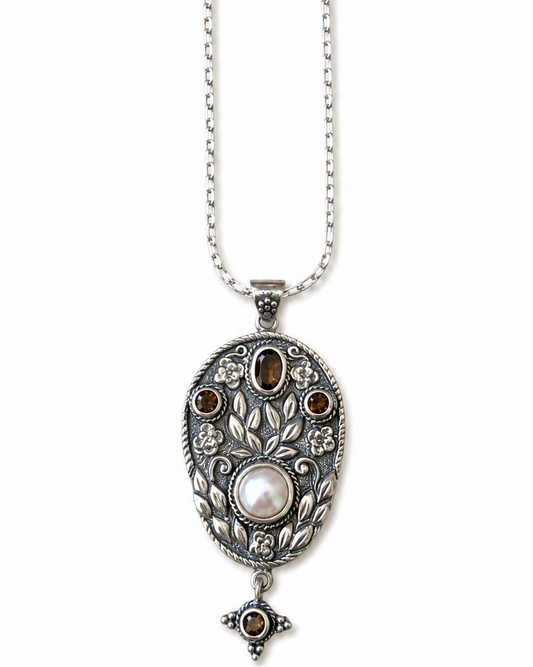Silver necklace with an ornate pendant featuring a central pearl and embedded stones on a white background.
